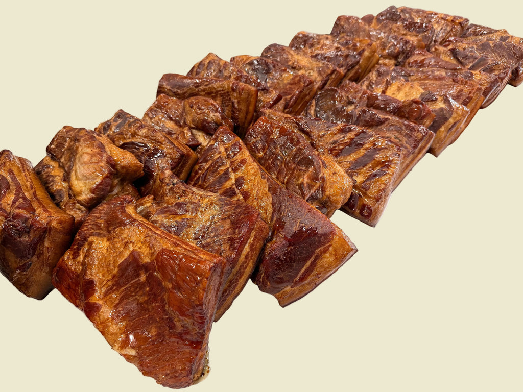 Several large glazed meat cuts, likely pork shoulder or brisket, arranged on a white paper-covered table in a commercial kitchen setting.