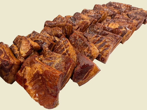 Several large glazed meat cuts, likely pork shoulder or brisket, arranged on a white paper-covered table in a commercial kitchen setting.