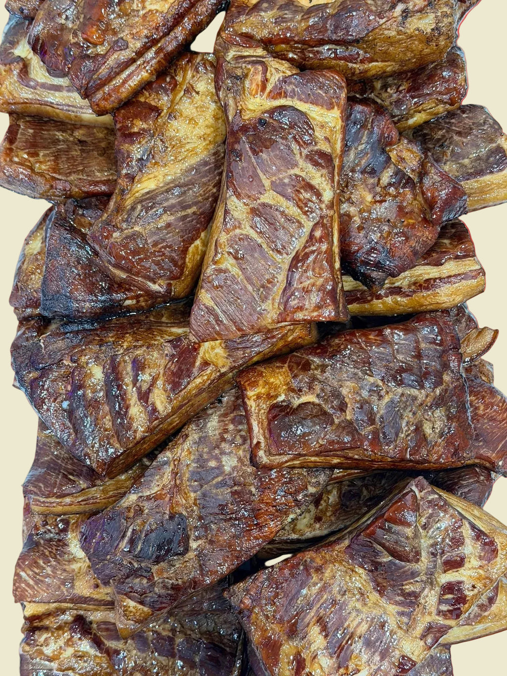 A close-up stack of glazed, marbled meat pieces with dark brown and golden-brown tones, filling the frame against a light blue background.
