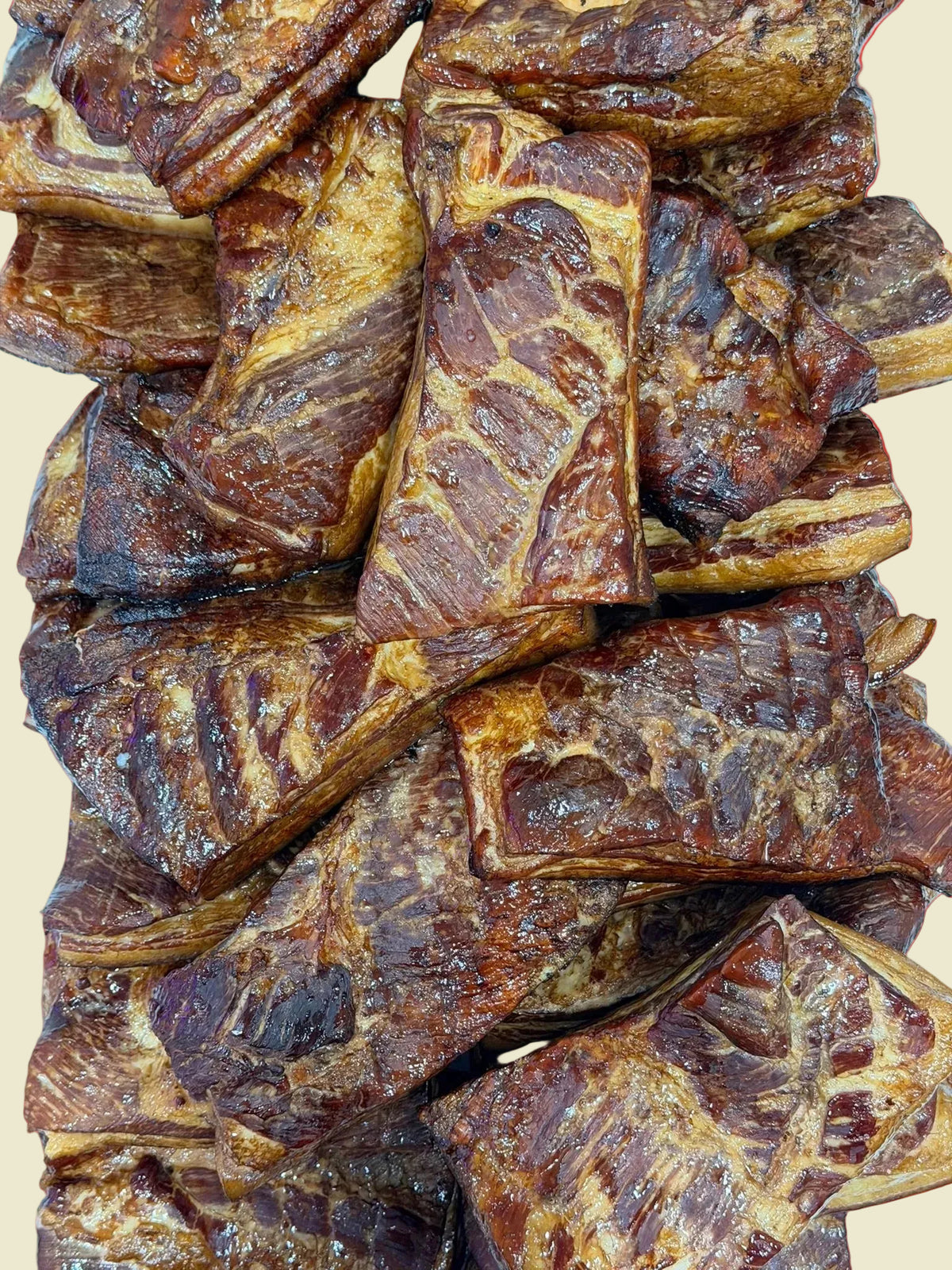 A close-up stack of glazed, marbled meat pieces with dark brown and golden-brown tones, filling the frame against a light blue background.